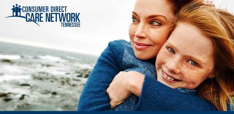 Mother and daughter smiling on the shore of a lake.